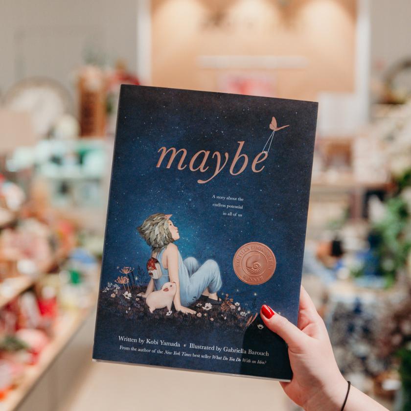 A children's book called Maybe with a dark blue cover and a child on the cover, sitting next to a pig looking up at the sky