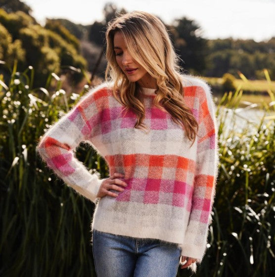 Blondw woman wearing angora orange and pink check sweater and blue jeans.