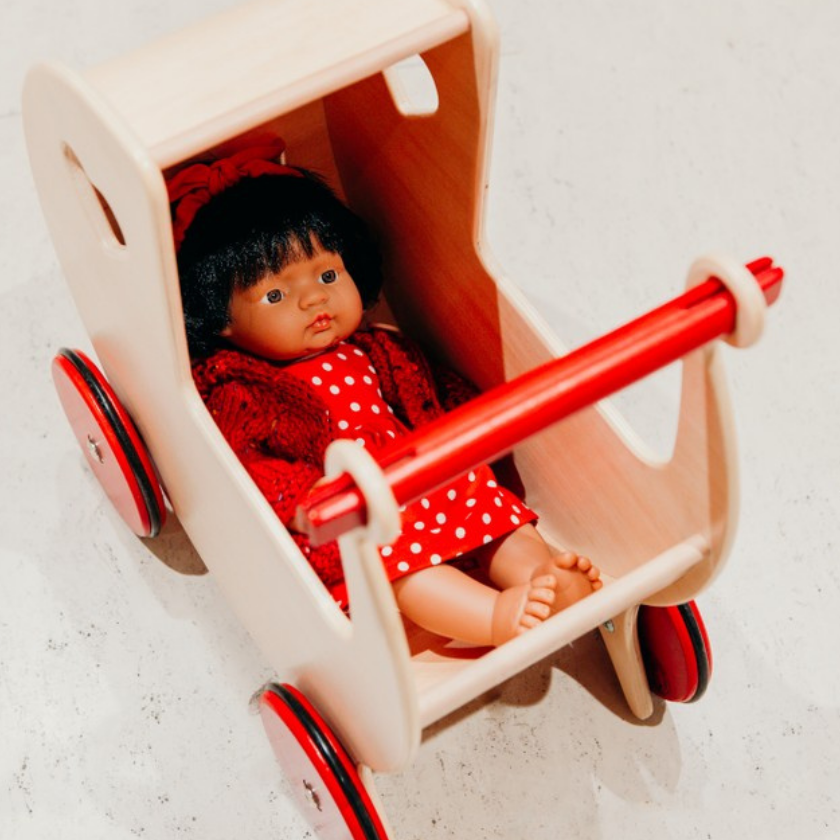 Miniland doll in red dress in a wooden pram
