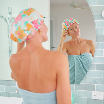 Linen shower cap in hibiscus by Annabel Trends on model, who is looking in the mirror, wearing a shower cap