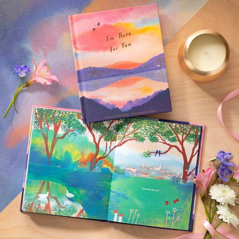 Colorful books with nature-themed designs on a wooden surface with flowers and a candle.
