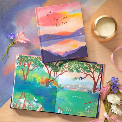 Colorful books with nature-themed designs on a wooden surface with flowers and a candle.