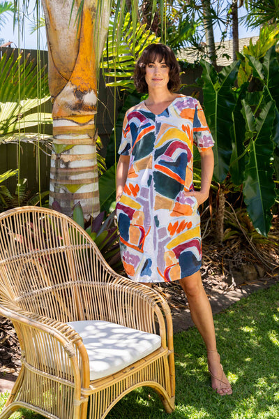 Woman in a colourful dress standing next to a wicker chair in a garden setting