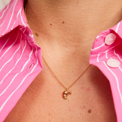 Gold necklace worn by a person with a pink shirt in the background By Tiger Tree