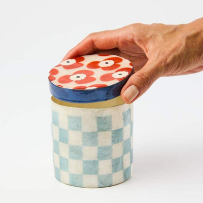Hand holding a decorative jar with a patterned lid on a white background
