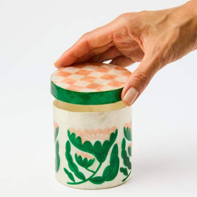 Hand holding a decorative jar with a checkered lid on a white background