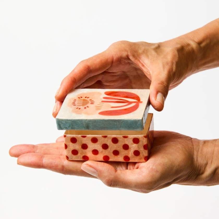 Two hands holding a small boxe with decorative designs on a white background