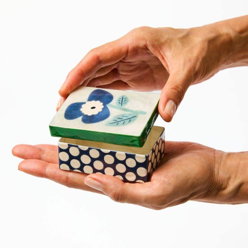Hand holding a stack of decorative boxes with floral and polka dot designs.