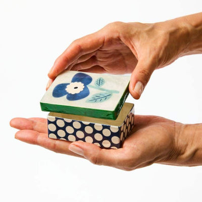Hand holding a stack of decorative boxes with floral and polka dot designs.