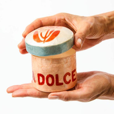 Person holding a small container labeled 'DOLCE' with a logo on a white background