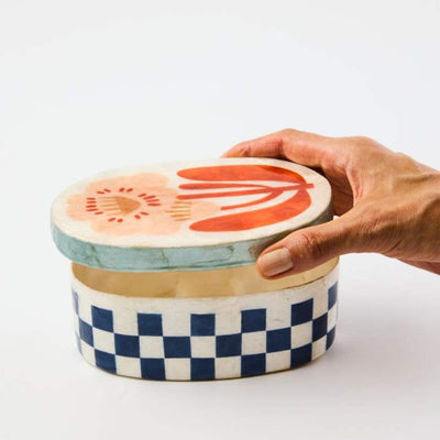 Hand holding a ceramic container with a checkered base and colorful lid.