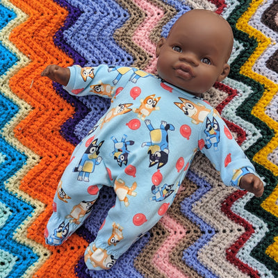 A 32cm soft body doll African Miniland doll wearing a blue onesie with Blue characters on it