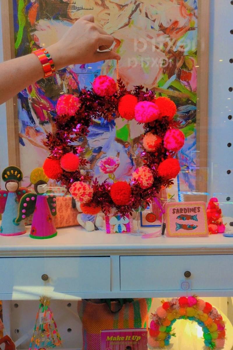 Colorful wreath with pink and red pom-poms on a display table with various items | Pom pom wreaths by Arissa Lifestyle are available at Zebra Finch in Newcastle NSW