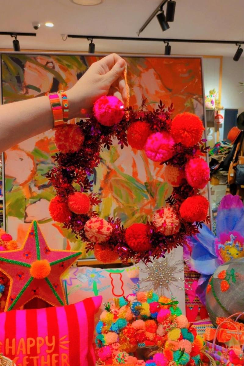 Colorful wreath with pink and red pom-poms on a display table with various items | Pom pom wreaths by Arissa Lifestyle are available at Zebra Finch in Newcastle NSW