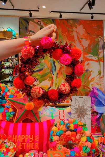 Colorful wreath with pink and red pom-poms on a display table with various items | Pom pom wreaths by Arissa Lifestyle are available at Zebra Finch in Newcastle NSW