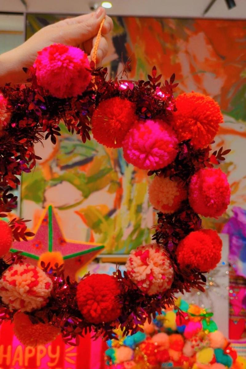 Colorful wreath with pink and red pom-poms on a display table with various items | Pom pom wreaths by Arissa Lifestyle are available at Zebra Finch in Newcastle NSW