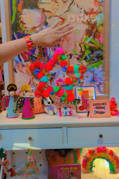 Colourful pom-pom wreath being held in front of a vibrant painting with various decorative items | Star pom pom wreath by Arissa available at Zebra Finch Style