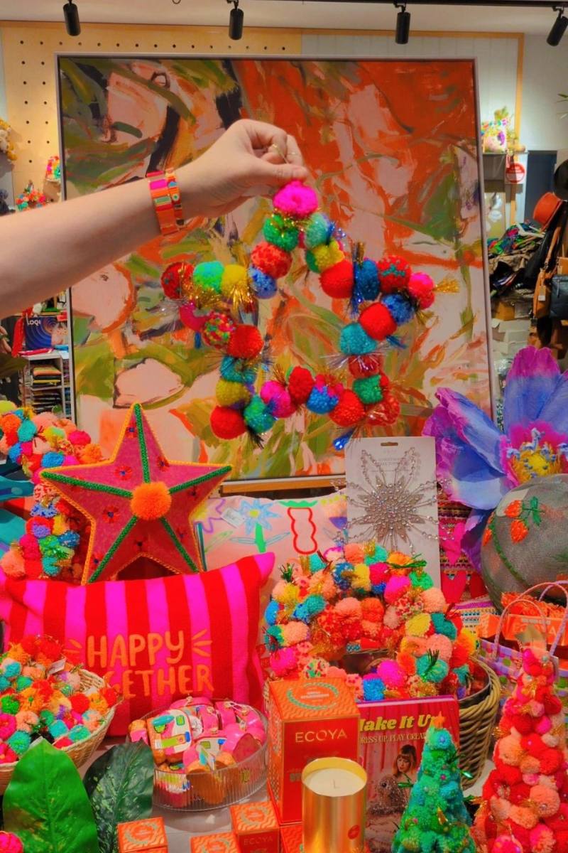 Colourful pom-pom wreath being held in front of a vibrant painting with various decorative items | Star pom pom wreath by Arissa available at Zebra Finch Style