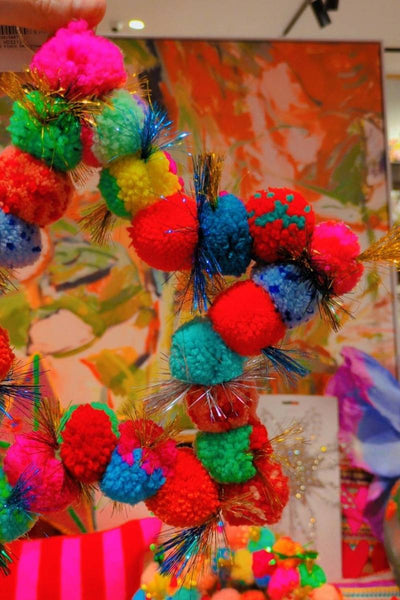 Colourful pom-pom wreath being held in front of a vibrant painting with various decorative items | Star pom pom wreath by Arissa available at Zebra Finch Style