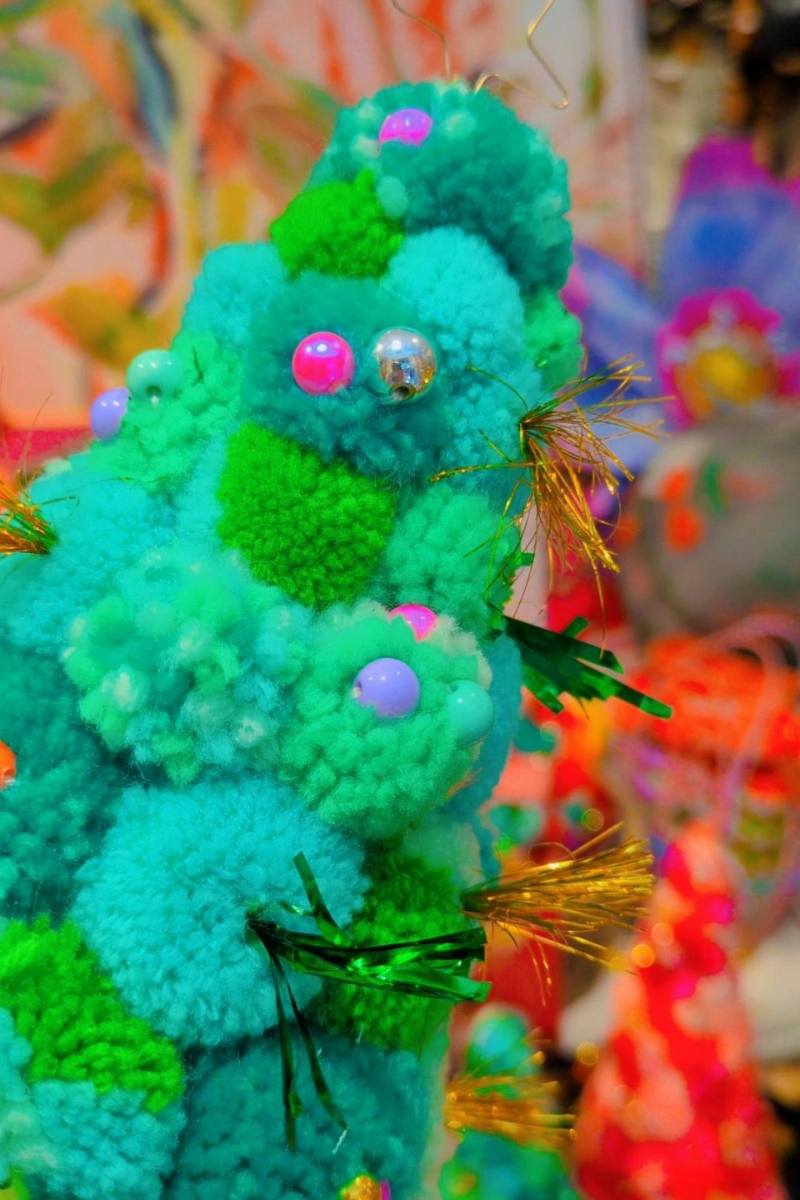 Colorful pom-pom tree held by a hand with a vibrant, multicolored background. | Pom pom wreaths and christmas trees by Arissa Lifestyle available at Zebra Finch in Newcastle, NSW