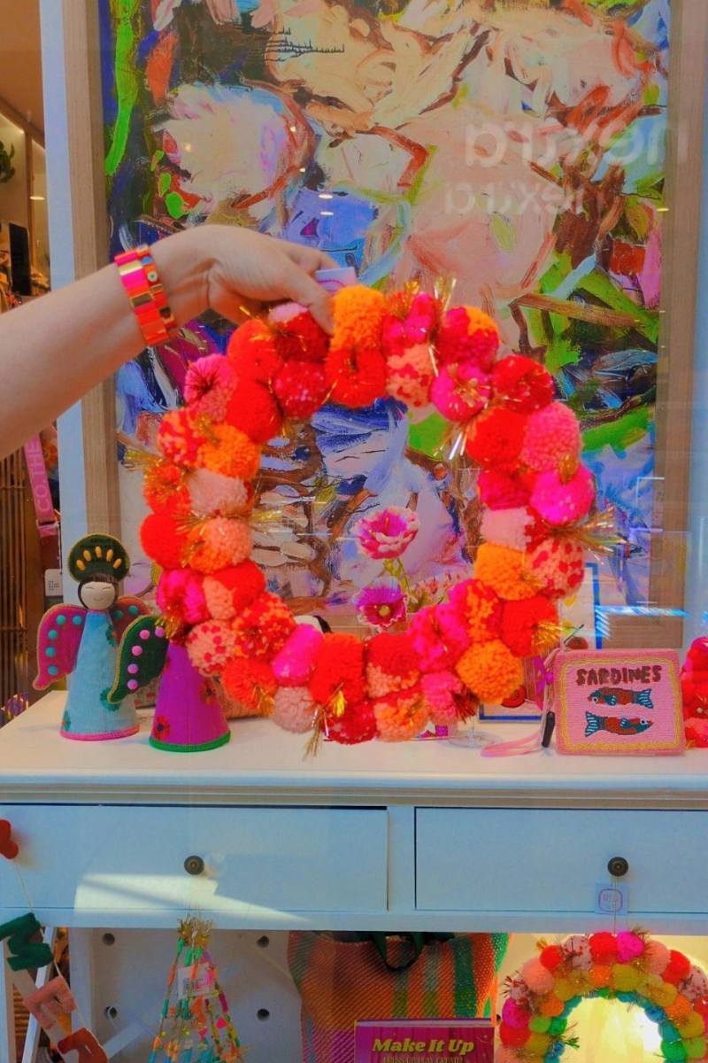 Colorful wreath held by a hand with a decorative background | Pink and orange handcrafted pom pom wreath by Arissa Lifestyle available at Zebra Finch in Newcastle, NSW