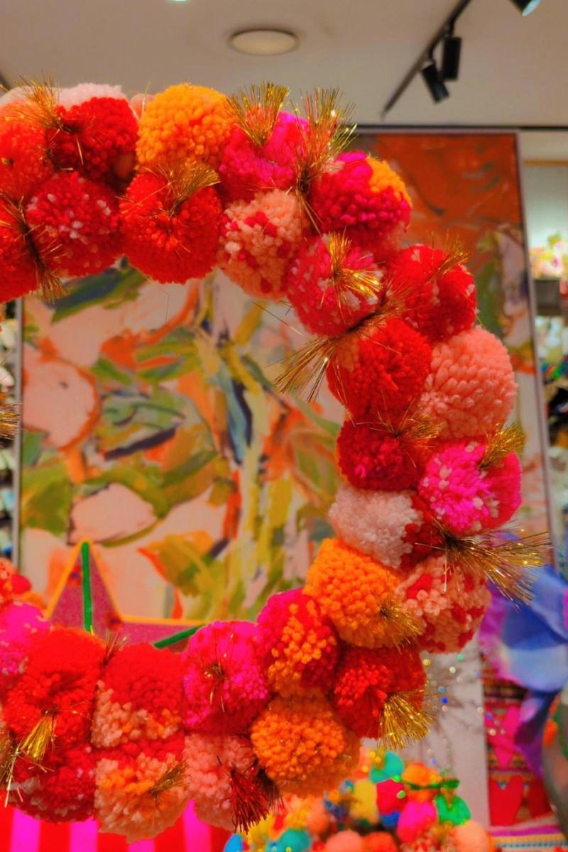 Colorful wreath held by a hand with a decorative background | Pink and orange handcrafted pom pom wreath by Arissa Lifestyle available at Zebra Finch in Newcastle, NSW