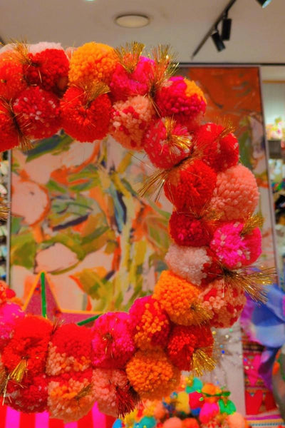 Colorful wreath held by a hand with a decorative background | Pink and orange handcrafted pom pom wreath by Arissa Lifestyle available at Zebra Finch in Newcastle, NSW