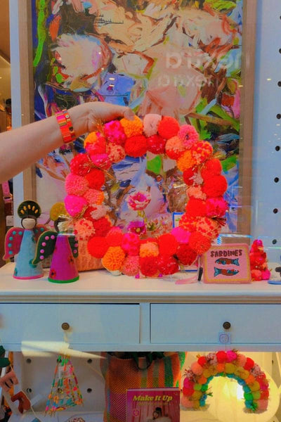 Colorful wreath held by a hand with a decorative background | Pink and orange handcrafted pom pom wreath by Arissa Lifestyle available at Zebra Finch in Newcastle, NSW