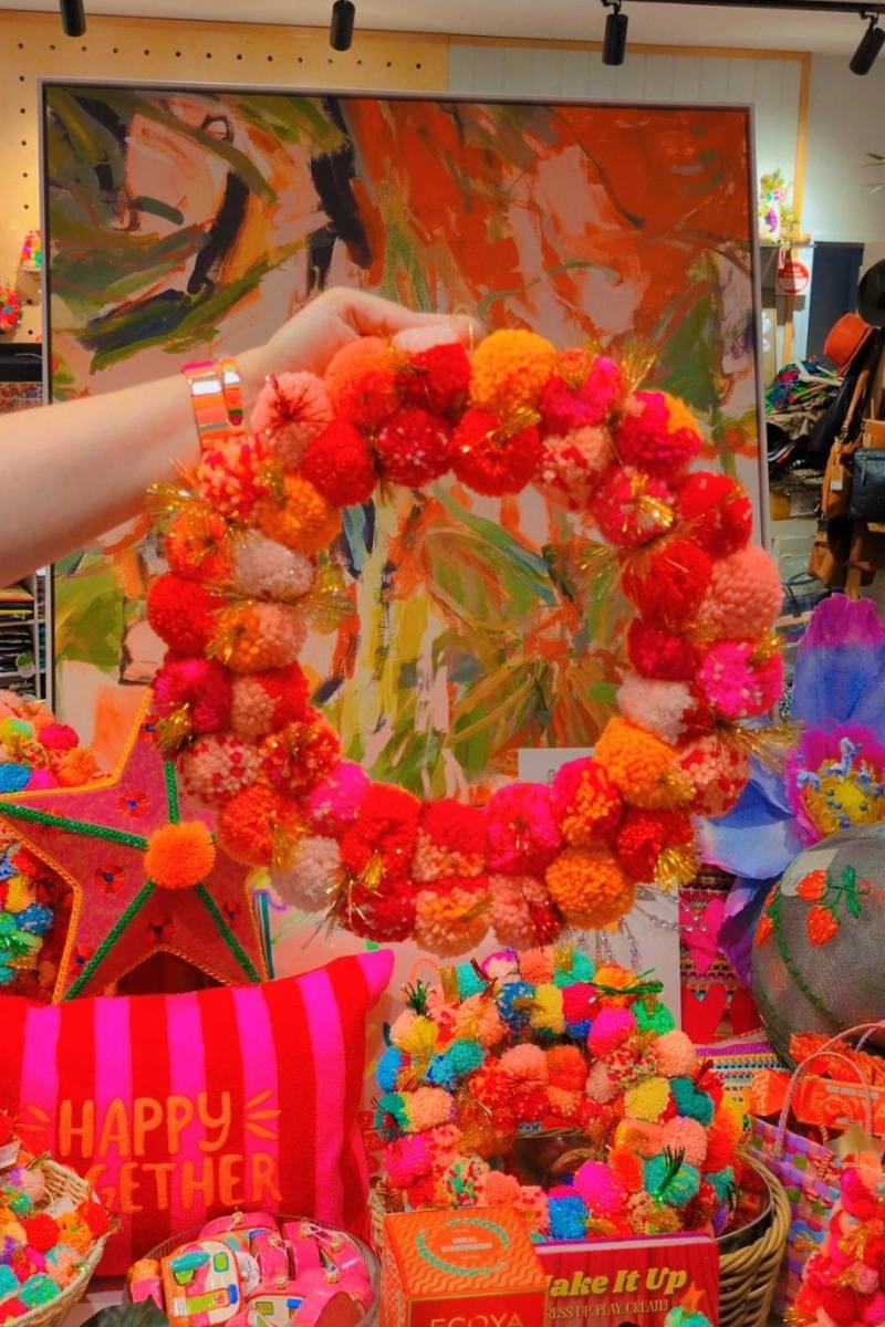 Colorful wreath held by a hand with a decorative background | Pink and orange handcrafted pom pom wreath by Arissa Lifestyle available at Zebra Finch in Newcastle, NSW
