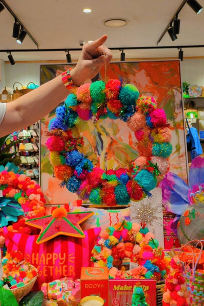 Colorful pom-pom wreath against a vibrant floral backdrop | Arissa pom pom wreaths available at Zebra Finch