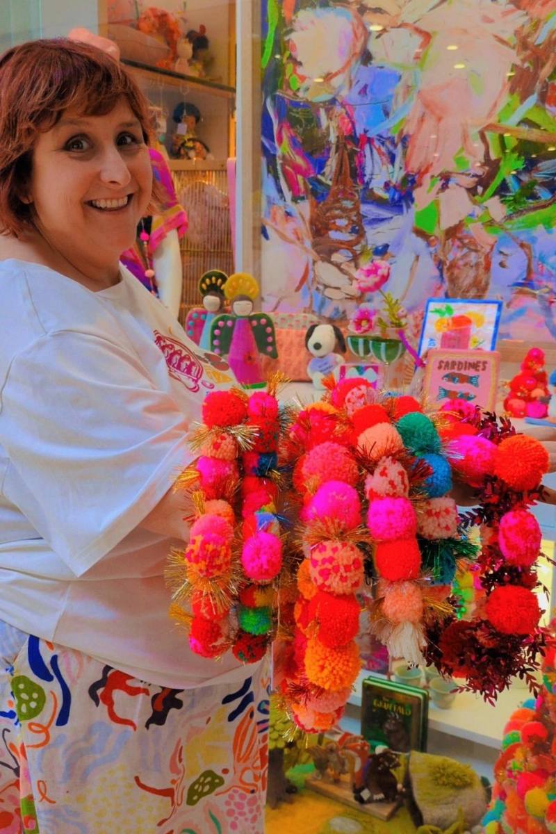 Colorful wreath held by a hand with a vibrant painting in the background | Arissa rainbow pom pom wreaths available at Zebra Finch in Newcastle, NSW