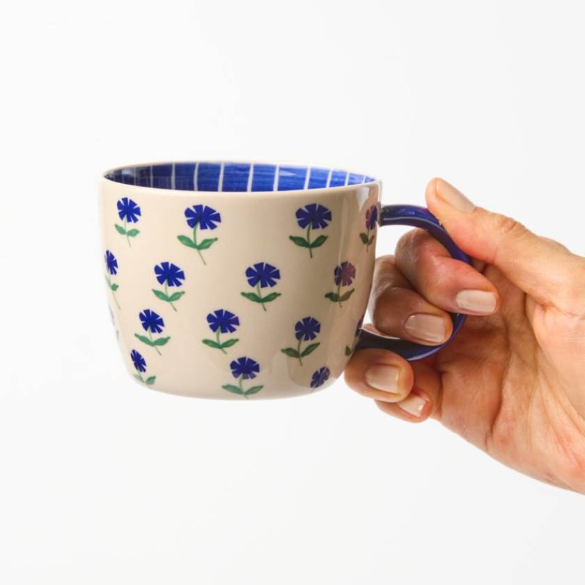 Hand holding a mug with floral pattern on a white background