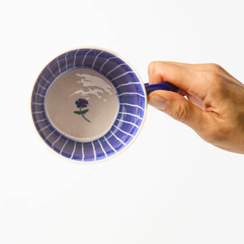 Ceramic mug with blue rim and floral design held by a hand on a white background