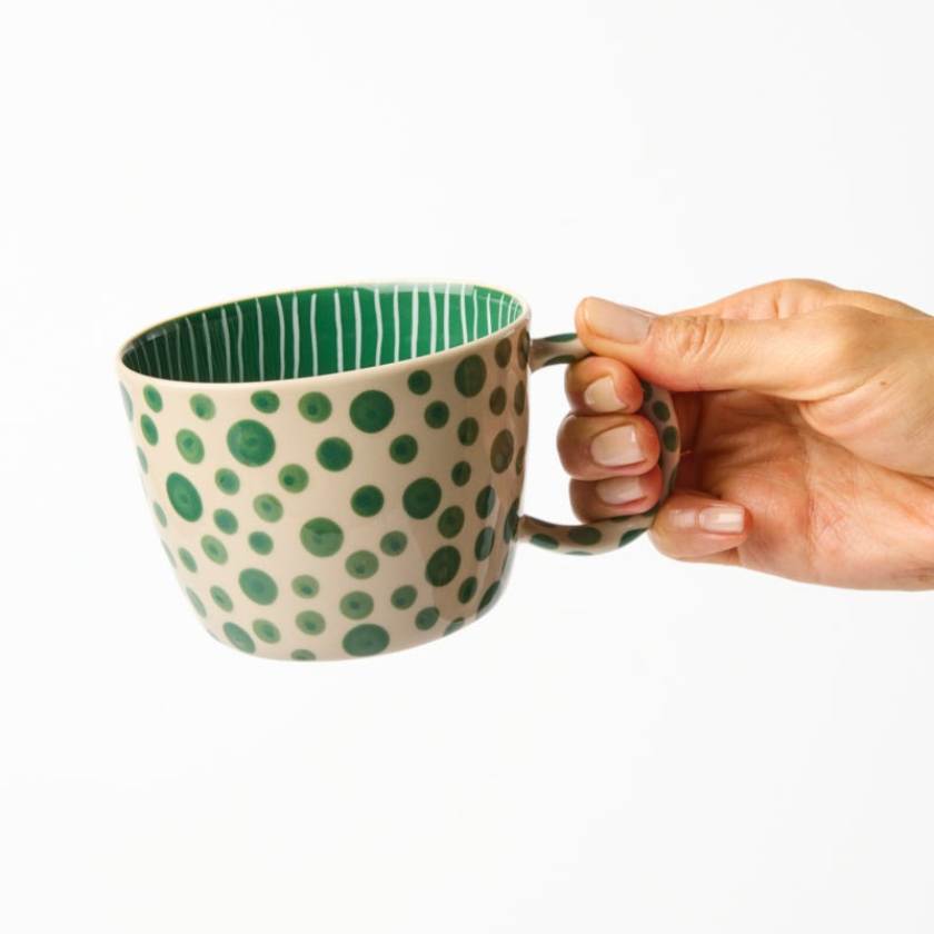 Hand holding a ceramic mug with green polka dot design on a white background