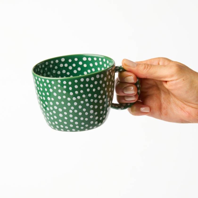 Hand holding a green mug with white polka dots on a white background