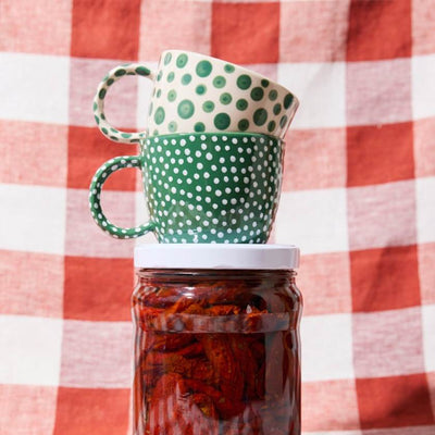 Green polka dot mugs stacked on a jar against a red and white checkered background