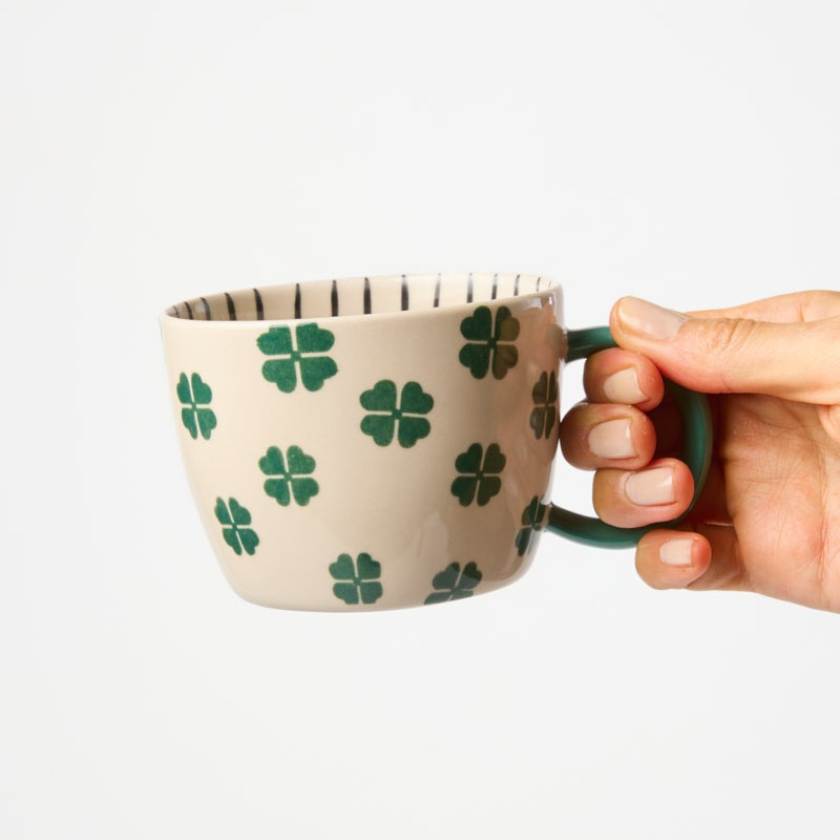 Hand holding a mug with clover pattern on a white background
