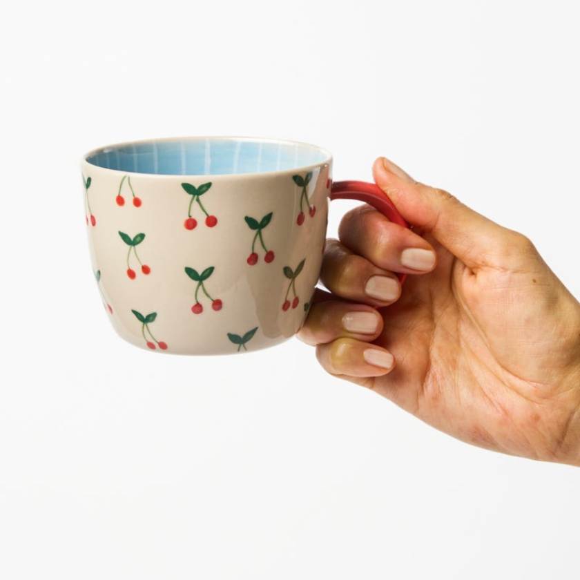 Hand holding a mug with cherry pattern on a white background