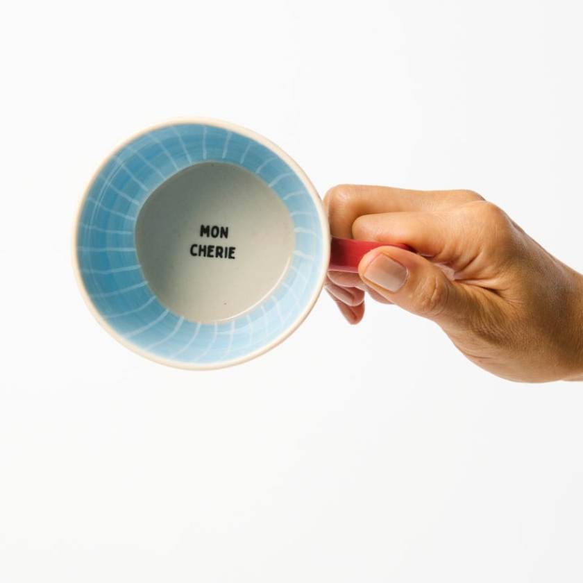 Hand holding a mug with 'MON CHERIE' text on a white background