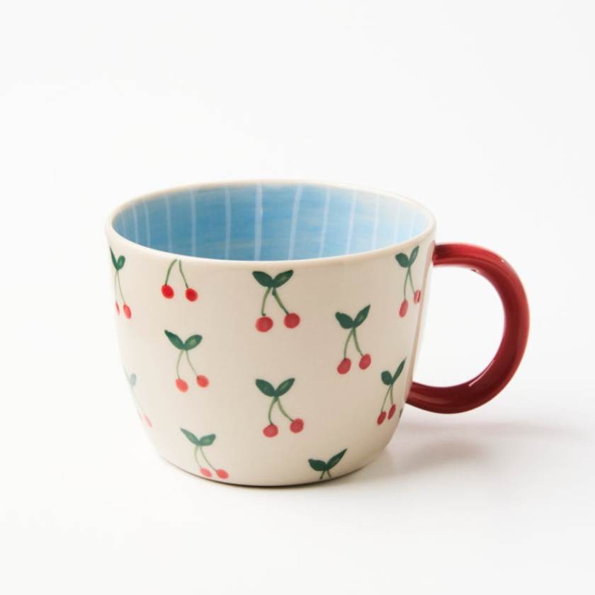 Ceramic mug with cherry pattern and red handle on a white background