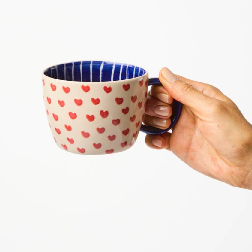 Hand holding a mug with red heart pattern on a white background