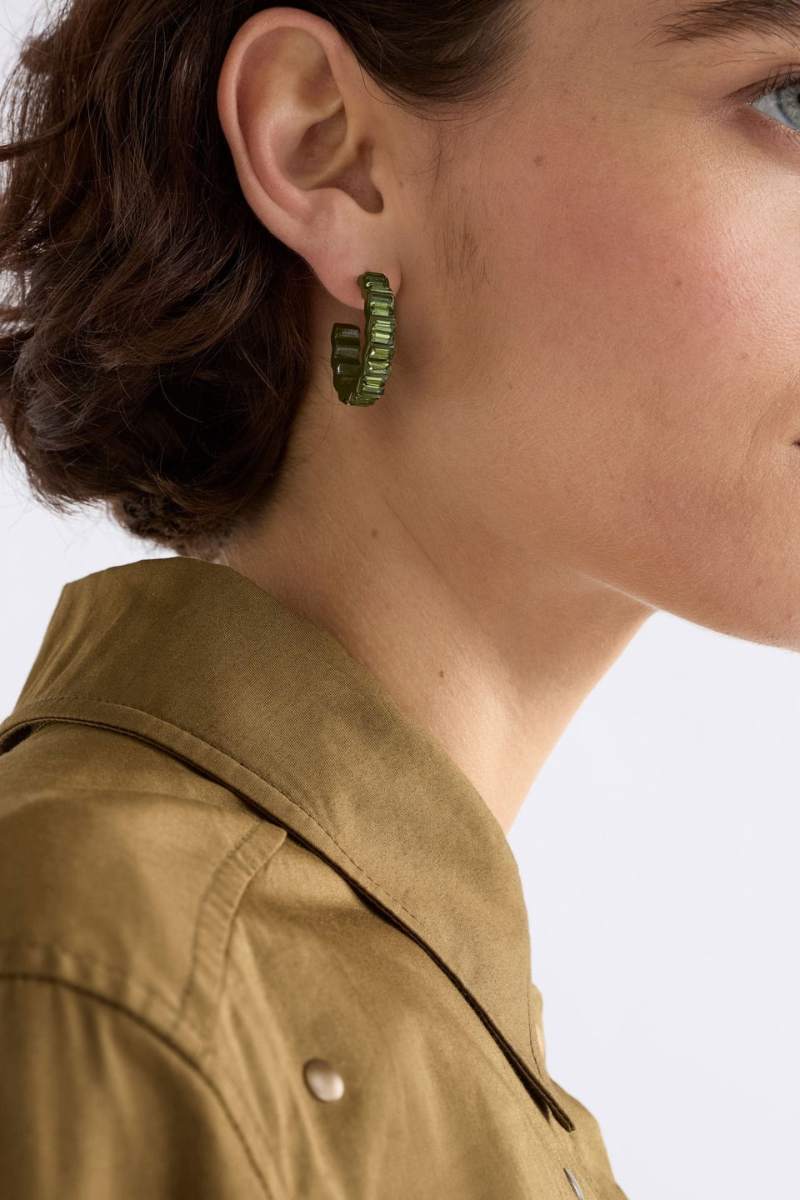 Close-up of a person wearing green hoop earrings with a neutral background
