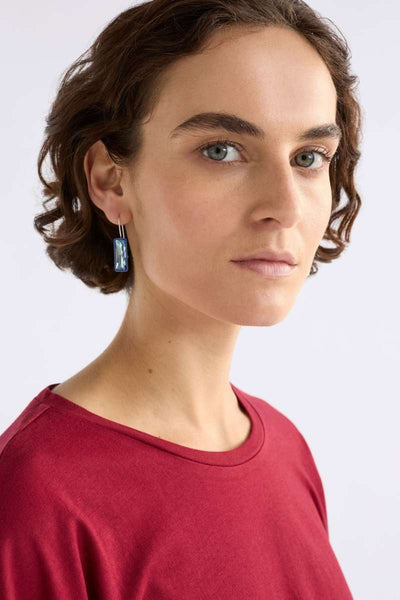 Woman wearing a red top with a plain background - Pair of blue earrings on a white background - Jule Small Hook Earrings by ELK. ELK Stockist at Newcastle, NSW at Zebra Finch