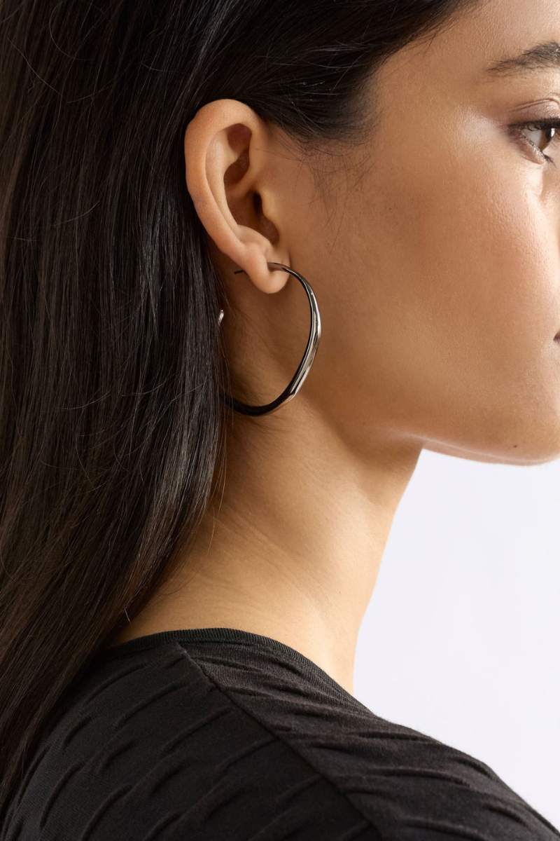 Close-up of a person wearing a silver hoop earring against a neutral background