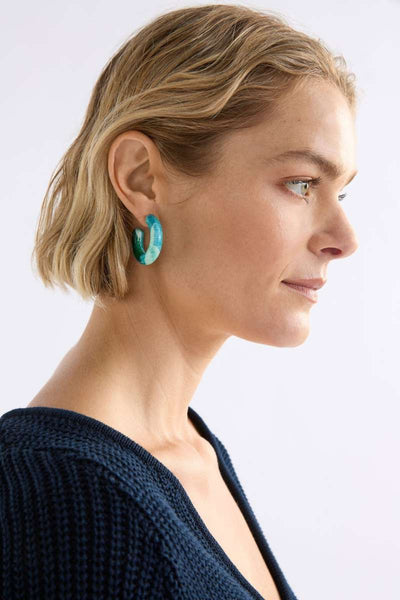 Woman wearing turquoise earrings with a plain background. Close-up of a person wearing turquoise hoop earrings with a neutral background. Resso Hoop Earring by ELK the Label. ELK Stockist in Newcastle, NSW at Zebra Finch Style