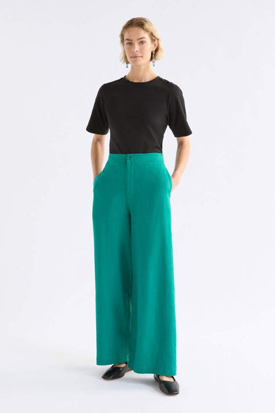 Woman wearing a black top and teal pants on a white background