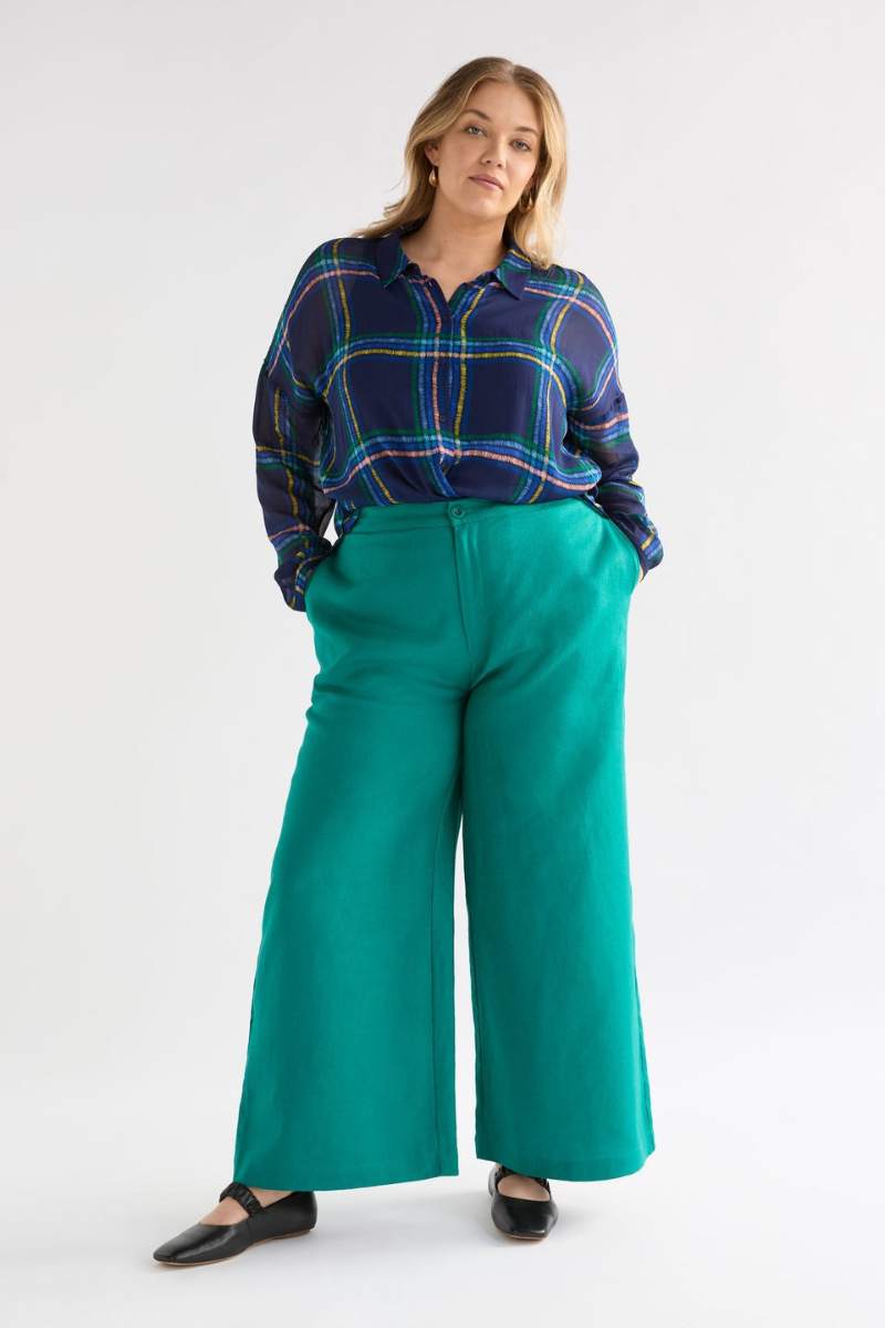 Woman wearing a plaid shirt and teal wide-leg pants on a white background