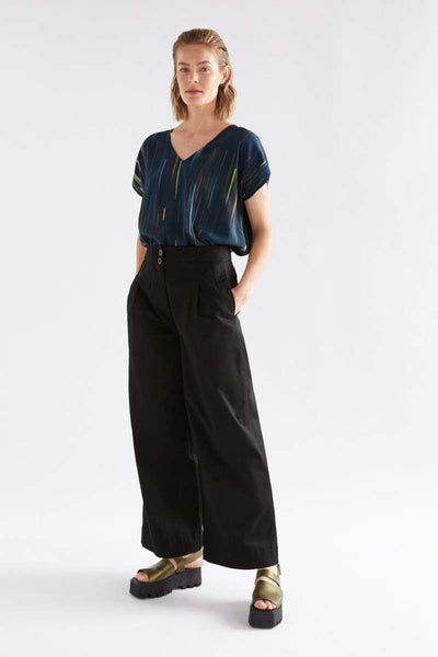 Woman wearing a dark blue top and black wide-leg pants on a white background