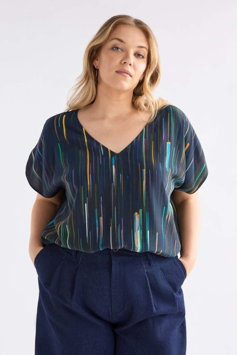 Woman wearing a patterned top and navy pants against a white background