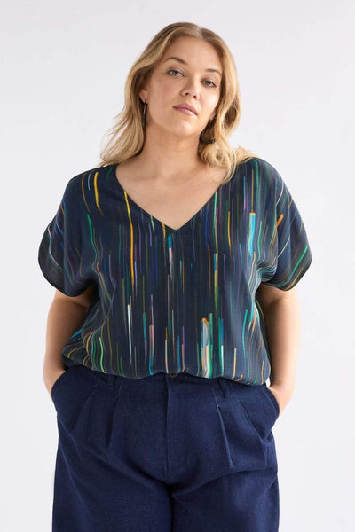 Woman wearing a patterned top and navy pants against a white background
